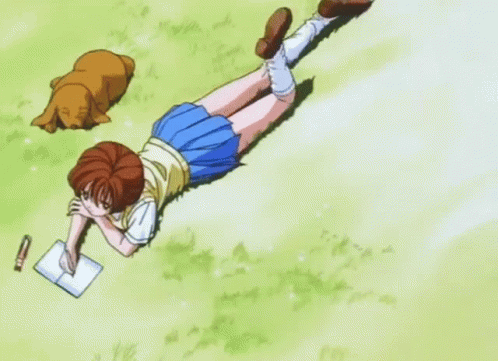 a girl is laying on the grass writing in a notebook while a dog naps to the side